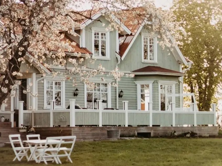green house with white trim, a white porch railing, and cherry blossoms on a sage cottage at golden hour
