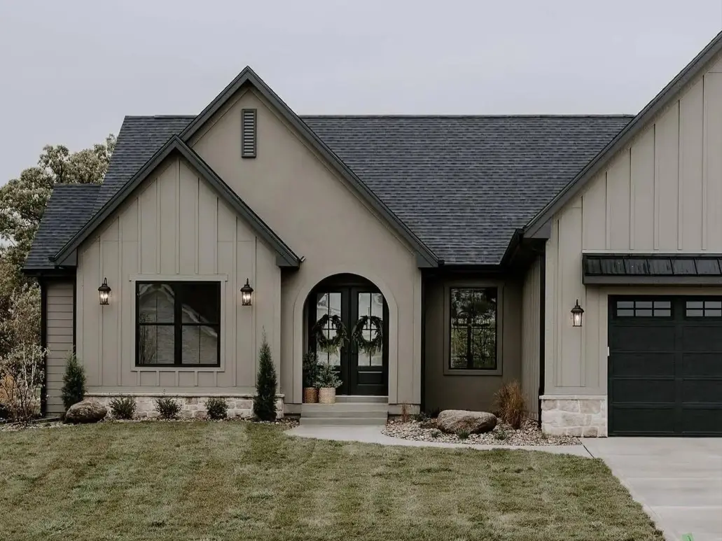 Taupe house with black trim, greige board-and-batten and stucco with a black arched door, black windows, and a stone base