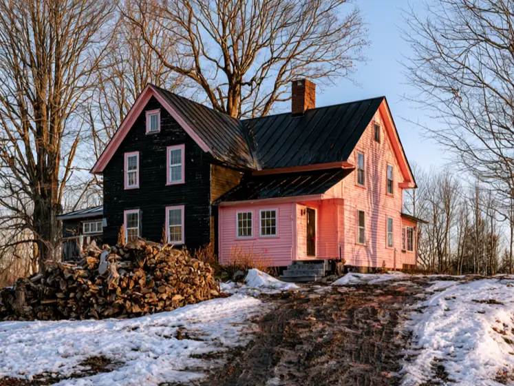 Black and pink houses: a two-tone farmhouse with a black clapboard wing, pink window trim, and a pink wing under a black metal roof in winter